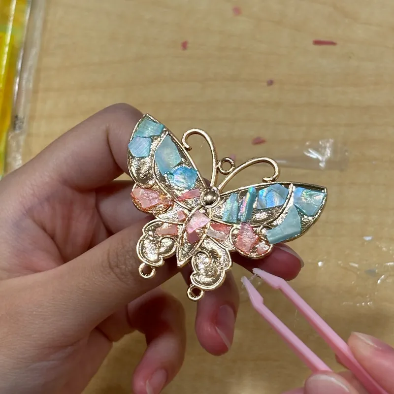 A gold filigree butterfly hairpin inlaid with pastel shell, held in one hand