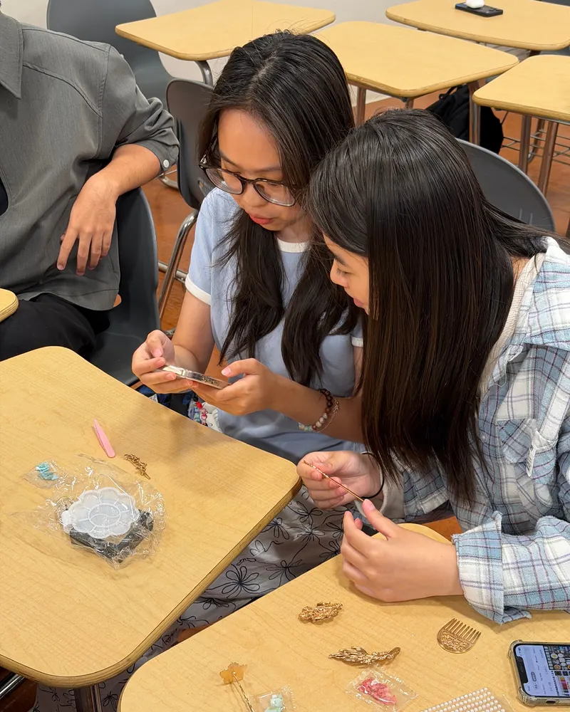 Two members bent over a desk assembling inlaid hairpins