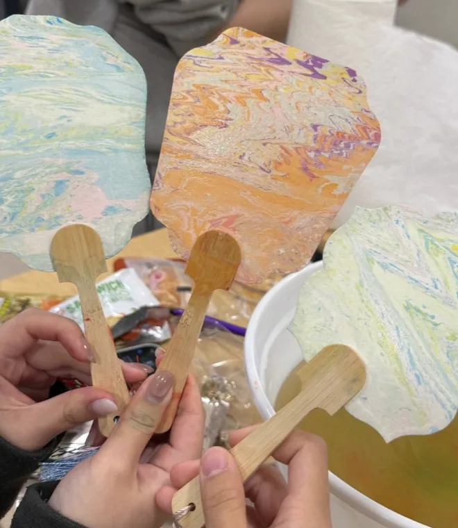 Hands holding freshly marbled lacquer fans over the dipping bowl